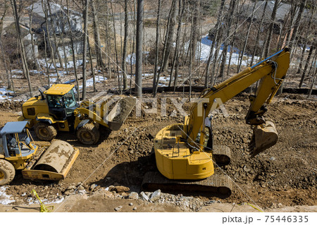 Under construction of a new asphalt road. The excavators, graders and road rollers working on the new road construction Under construction of a new asphalt road. The excavators, graders and road rollers working on the new road construction 75446335