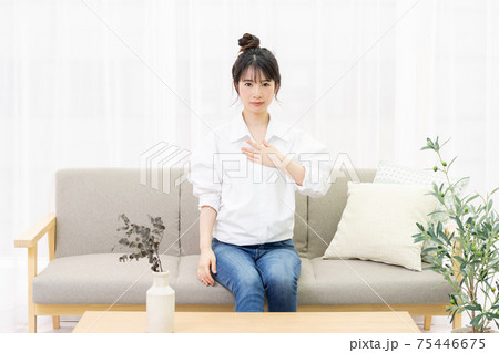 窓際のソファに座って胸に手を置く若い女性 窓際のソファに座って胸に手を置く若い女性 75446675