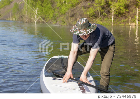 a country boy in rubber boots tries to stand on a sup board on the water, on the lake 75446979