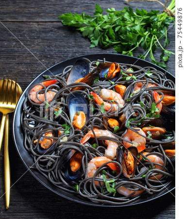 Squid ink spaghetti with seafood on a black plate Squid ink spaghetti with seafood on a black plate 75449876