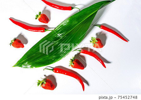 red chili peppers and ripe strawberries and green leaves on a white background red chili peppers and ripe strawberries and green leaves on a white background 75452748