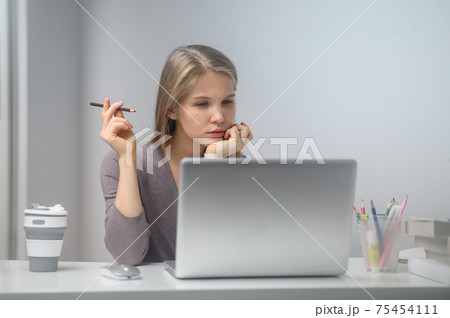 A girl with a laptop is studying at an online school. White room background A girl with a laptop is studying at an online school. White room background 75454111