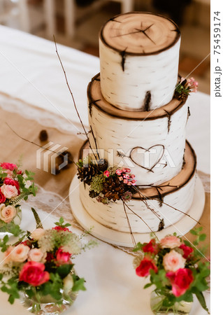 Wedding 3-storey cake that imitates pieces of tree trunk-birch. Cake complemented by natural decorations(cones,branches,flowers). On cake is carved heart pierced by arrow. Focused on center of cake. 75459174