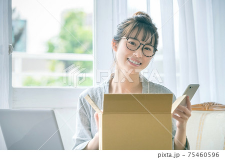 自宅で荷物を確認するスマホを持った若いパジャマ姿の女性 75460596