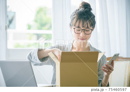 自宅で荷物を確認するスマホを持った若いパジャマ姿の女性 75460597