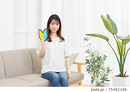 ソファに座って初心者マークを手に持つ若い女性 75462199