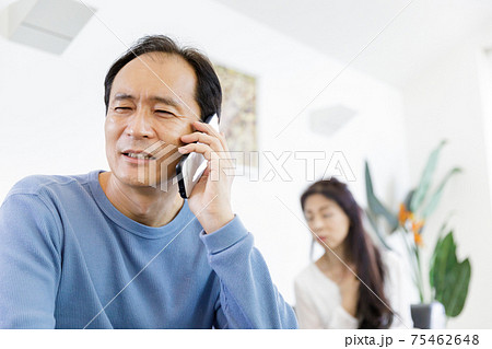 電話で通話をしている男性と会話が気になる女性の写真素材