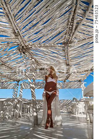 Attractive young woman wearing swimsuit and pareo standing over white bamboo wall 75463523