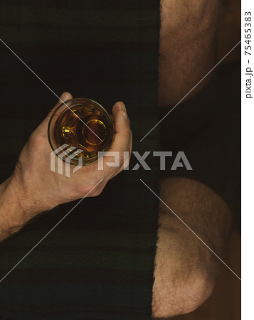 Irish man in green kilt celebrating St. Patrick's Day with scotch drink glass in hand Scottish guy drinks whiskey in pub 75465383