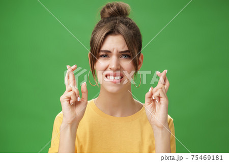 Close-up shot of nervous woman praying for having positive answer crossing fingers for good luck biting lower lip anxiously and frowning being worried while hoping to get job over green background Close-up shot of nervous woman praying for having positive answer crossing fingers for good luck biting lower lip anxiously and frowning being worried while hoping to get job over green background 75469181