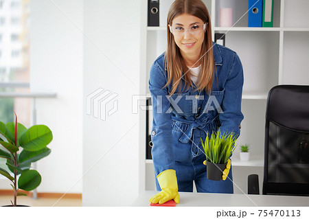 Pretty woman in uniform with supplies cleaning in office Pretty woman in uniform with supplies cleaning in office 75470113