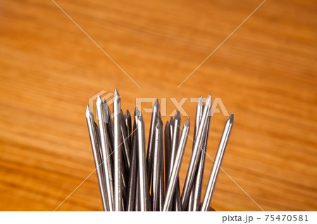 Metal iron pointed nail on walnut wood in, isolated on wooden background Metal iron pointed nail on walnut wood in, isolated on wooden background 75470581