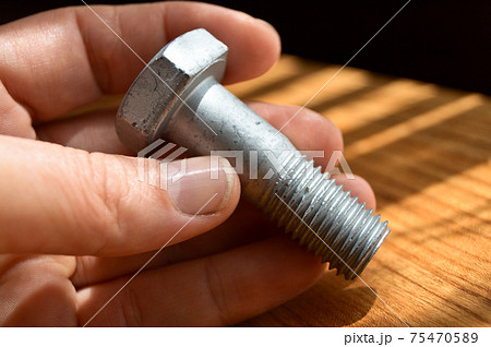 Galvanized metal with metric bolt and hand, isolated on brown walnut wood 75470589