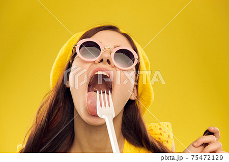 Happy woman in a yellow hat and fashionable glasses holds her hands near her face on a yellow background cropped view of emotions fun 75472129