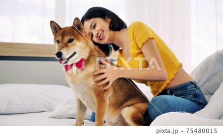 Happy woman and shiba inu dog lying together on a bed at home 75480015