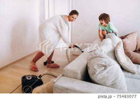 the mother vacuums the floor at home and the son watches and laughs at it the mother vacuums the floor at home and the son watches and laughs at it 75483077