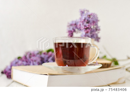 Romantic background with a cup of tea, lilac flowers and a book over a white wooden table. Leisure concept, spring breakfast. 75483406