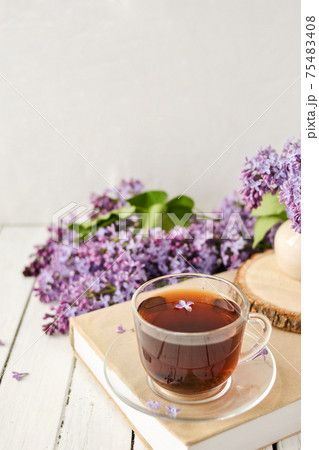 Romantic background with a cup of tea, lilac flowers and a book over a white wooden table. Leisure concept, spring breakfast. 75483408