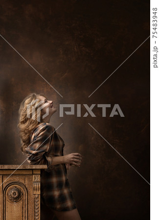 Pretty woman with long blonde hair in brown plaid shirt holds coffee cup and looks up . 75483948