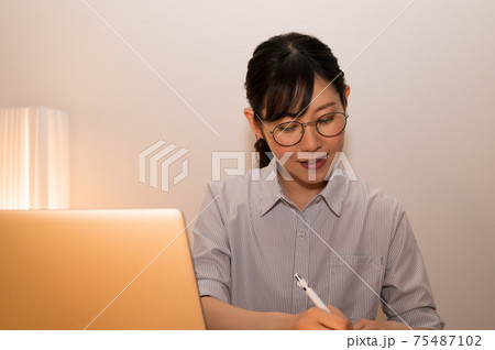 夜にパソコンで勉強しながらノートにメモ書きする女性 75487102