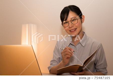 夜にパソコンで勉強しながらノートにメモ書きする女性 夜にパソコンで勉強しながらノートにメモ書きする女性 75487105