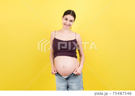 Happy pregnant woman in unzipped jeans showing her naked belly at colorful background with copy space. Baby expecting concept Happy pregnant woman in unzipped jeans showing her naked belly at colorful background with copy space. Baby expecting concept 75487546