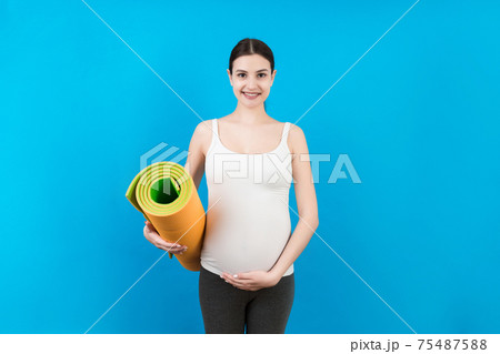 Pregnant Girl Holding Yoga Mat Standing Over Colored Background. Studio Shot, Free Space For Design 75487588