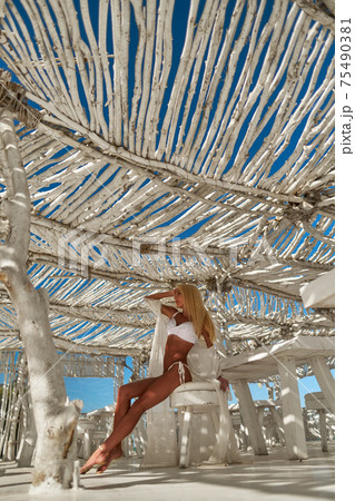 Attractive young woman wearing swimsuit and pareo standing over white bamboo wall 75490381