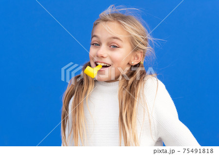 Studio portrait of a happy, smiling young girl celebrating birthday party, holding party blower in 75491818