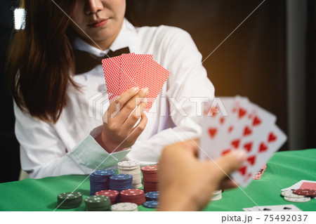 Women dealer or croupier shuffles poker cards in a casino on the background of a table, poker game concept 75492037