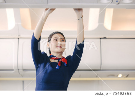 The stewardess helps the passengers to put their luggage in the cabin of the plane. Stewardess in the airplane. 75492368