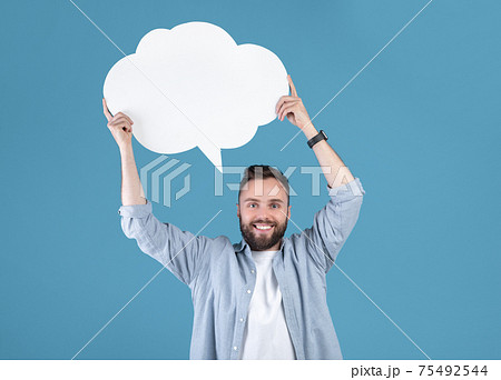 Millennial hipster guy holding speech bubble on blue studio background, mockup for design Millennial hipster guy holding speech bubble on blue studio background, mockup for design 75492544