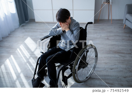 Above view of handicapped adolescent in wheelchair crying at home. Depression and loneliness in disabled teens concept 75492549