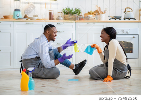Cheerful black couple chatting to each other on kitchen floor after domestic cleanup, full length portrait Cheerful black couple chatting to each other on kitchen floor after domestic cleanup, full length portrait 75492550