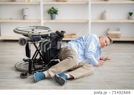 Senior man with physical disability lying on floor after falling down from his wheelchair at home 75492666