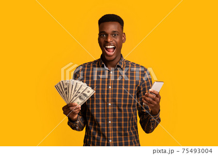 Online credit. Funny young black man holding smartphone and dollar cash Online credit. Funny young black man holding smartphone and dollar cash 75493004
