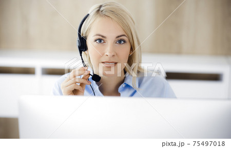 Blonde business woman sitting and communicated by headset in call center office. Concept of telesales business or home office occupation 75497018