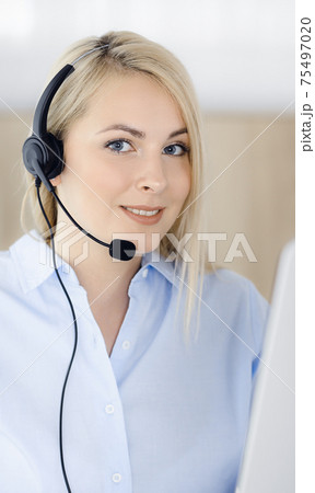 Blonde business woman sitting and communicated by headset in call center office. Concept of telesales business or home office occupation 75497020