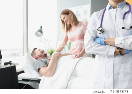 Happy man lies on hospital bed his hand is held by woman next to doctor Happy man lies on hospital bed his hand is held by woman next to doctor 75497373