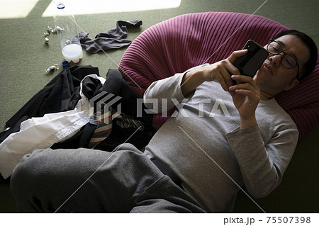 寝ながらスマホを見るだらしない男性 75507398