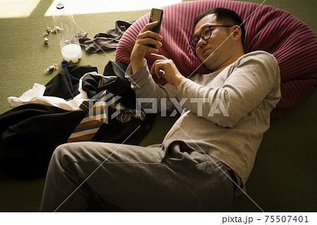 寝ながらスマホを見るだらしない男性 寝ながらスマホを見るだらしない男性 75507401