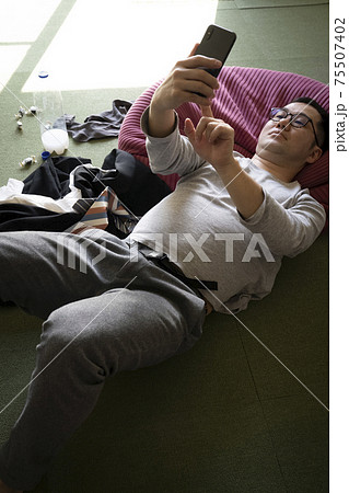 寝ながらスマホを見るだらしない男性 75507402
