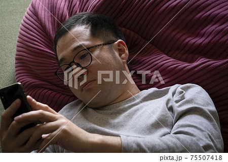 寝ながらスマホを見る男性 75507418