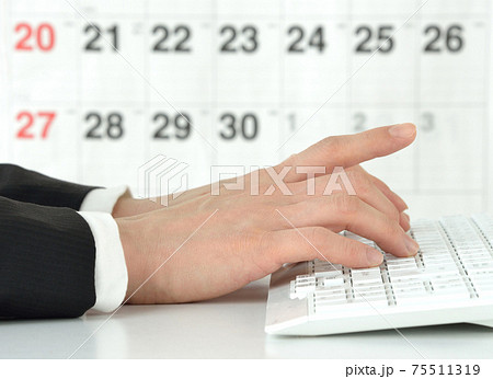 カレンダーの前でパソコン作業を行うビジネスマンの手 75511319