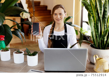 A florist girl uses her phone to take orders online at a flower shop. A florist girl uses her phone to take orders online at a flower shop. 75512914