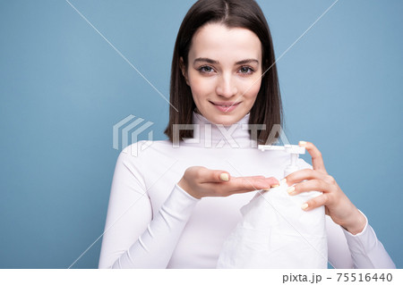 Young girl sanitizer in hands in the studio on a blue background. Hand disinfection and germ prevention. 75516440