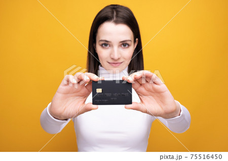 Close up portrait of young smiling business woman holding credit card, isolated on yellow background. 75516450