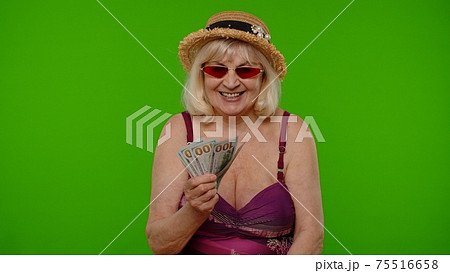 Rich senior woman tourist with cash fan enjoying financial independence waving currency dollar bills Rich senior woman tourist with cash fan enjoying financial independence waving currency dollar bills 75516658
