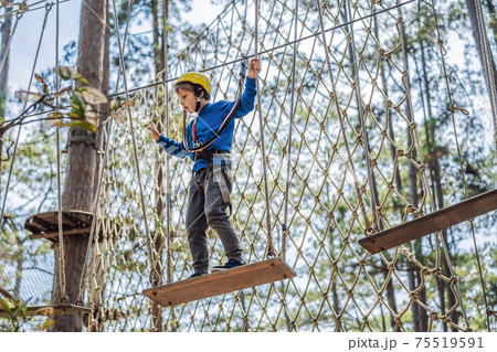 Happy child in a helmet, healthy teenager school boy enjoying activity in a climbing adventure park on a summer day Happy child in a helmet, healthy teenager school boy enjoying activity in a climbing adventure park on a summer day 75519591