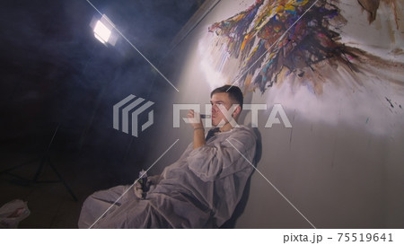Artist designer draws an eagle on the wall. Craftsman decorator paints a picture with acrylic oil color. Vaper smokes vape. Dark magic cinematic look. 75519641